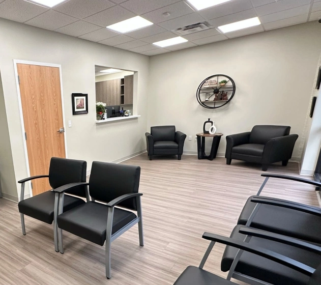 Modern dental office waiting room with black chairs, light wood flooring, and contemporary décor.